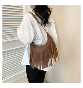 Dettaglio di una borsa a sella marrone con frange in finta pelle scamosciata su modella