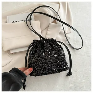 Detailed view of black sequin bucket bag with drawstring closure on textured fabric