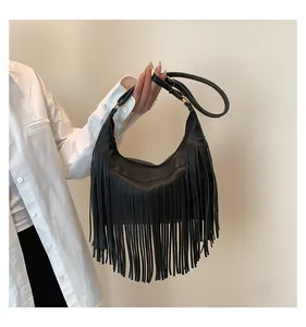 Dettaglio della borsa hobo nera con lunghe frange e tracolla regolabile su camicia bianca