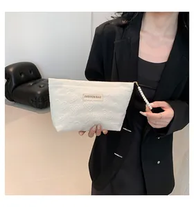 Detail einer weißen Handtasche mit Herzprägung, Perlenreißverschluss und Modelabel