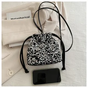 Detail of silver sequin bucket bag with drawstring closure next to a smartphone