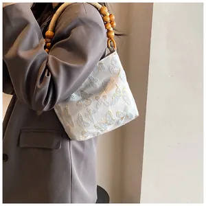 Detail der Schmetterlingsstickerei und Holzperlengriff an der weißen Schultertasche