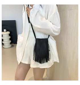 Detail shot of a black leather crossbody bag featuring bohemian style long tassels