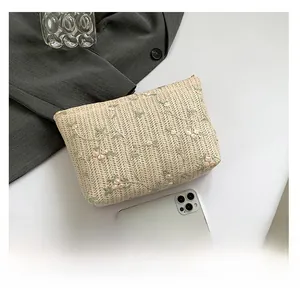 Close-up of beige woven clutch with floral embroidery next to a smartphone for scale