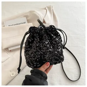 Detail of a black sequined drawstring bucket bag held by hand against a white suit