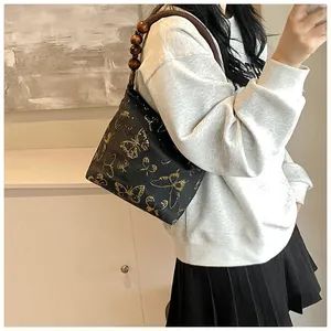 Details der schwarzen Vintage-Schultertasche mit goldenen Schmetterlingen und Holzperlengriff
