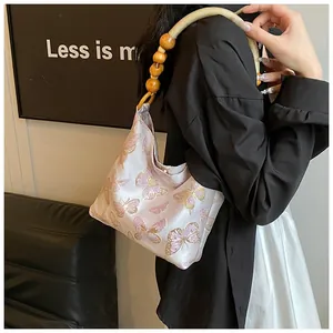 Detail der Hobo-Tasche mit Schmetterlingsstickerei und Webgriff mit Holzperlen
