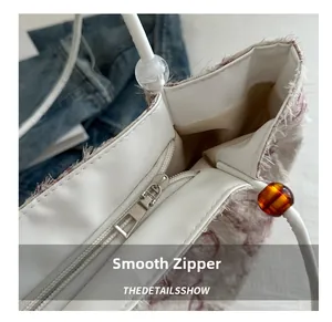 Detail of a white tweed tote bag showing a smooth silver metal zipper and beaded handle