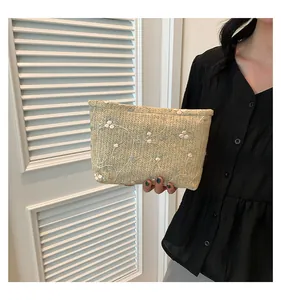 Detail of handwoven beige straw clutch featuring delicate pink floral embroidery