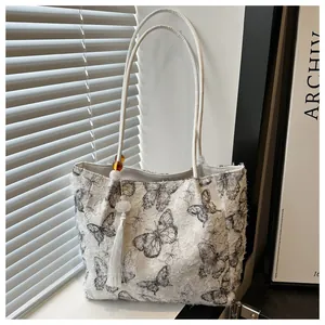 Detail of white tote bag with black butterfly prints, fringed edges, and beaded tassels