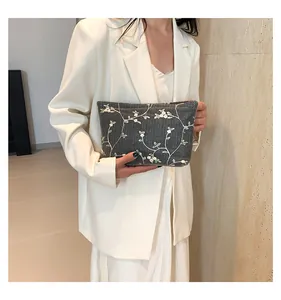 Detail of dark gray woven clutch bag with elegant white floral embroidery and branch pattern