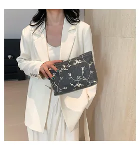 Detail of dark grey woven clutch bag with white floral embroidery held by model