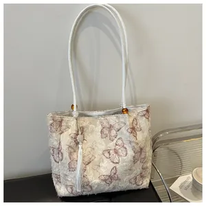 Detail of cream tote bag with butterfly embroidery, tassels, and amber bead accents