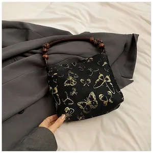Detail der schwarzen Jacquard-Handtasche mit goldener Schmetterlingsstickerei und Holzgriff
