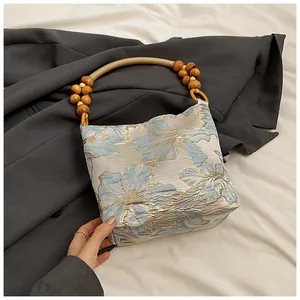 Detail der floralen Jacquard-Handtasche mit Perlengriff aus Holz auf grauem Anzug