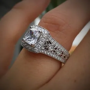 Close-up of square zircon ring with double halo and filigree engraved band on finger