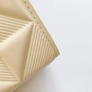 Detail van de crème lederen tas met diagonale reliëflijnen en strakke stiksels af