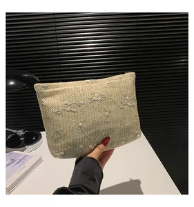 Close-up of beige woven clutch with floral embroidery held in hand with gold zipper detail