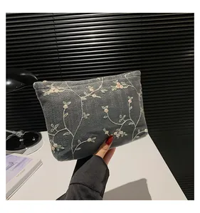 Close-up of pink floral embroidery and gold zipper on grey denim clutch bag