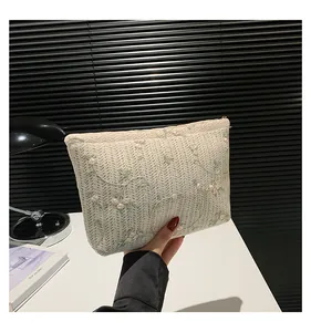 Detailed close-up of intricate lace embroidery and golden zipper on the beige clutch bag