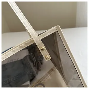 Detail view of transparent grey PVC tote bag with beige leather trim and golden rivets