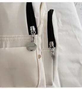 Close-up of smooth silver metal zipper pulls on a white canvas minimalist chest bag
