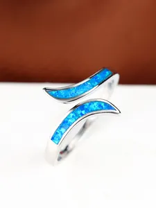 Macro shot of silver bypass ring with vibrant blue opal inlay and polished finish