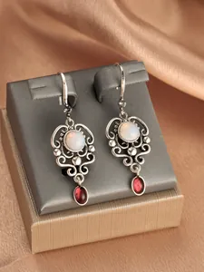 Detail of vintage silver hollow earrings with opal center and red teardrop gems