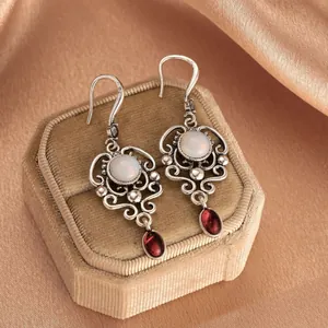 Vintage hollow silver earrings with white and red gemstones on a velvet jewelry box