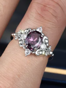 Close-up of a vintage oval purple gemstone ring with sparkling diamonds on a finger