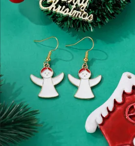 Close-up of golden angel drop earrings with white enamel on a festive green background