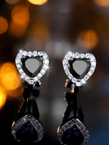 Gros plan de boucles d'oreilles en cœur avec pierre noire et halo blanc sur miroir noir