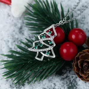 Macro shot of a sparkling silver Christmas tree pendant with green gems on a snowy branch