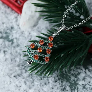 Close-up of hollow Christmas tree pendant with green gems and orange stones on silver chain