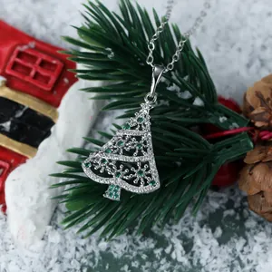 Close-up of hollow Christmas tree necklace with green stones and festive pine background