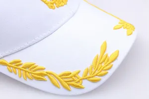 Detailed close-up of golden laurel leaf embroidery on the brim of a white cotton baseball cap