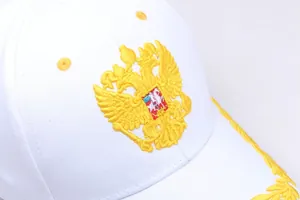 Detailed close-up of golden double-headed eagle embroidery on a white baseball cap