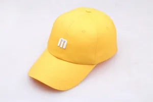 Détail d'une casquette en coton jaune avec broderie M blanche et coutures sur la visière