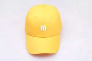 Détail de la broderie de la lettre m blanche sur le tissu en coton de la casquette jaune