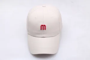 Détail de la broderie de la lettre M rouge sur une casquette de baseball en coton beige
