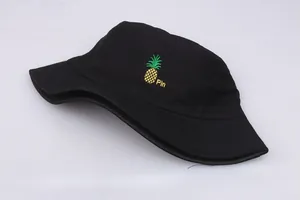 Detalle de un sombrero de pescador negro con bordado de piña amarilla y el texto 'Pin'