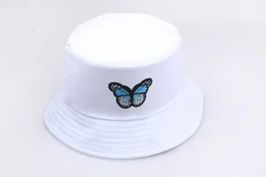Dettaglio del ricamo a farfalla blu su cappello pescatore in cotone bianco con tesa cucita