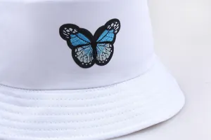 Dettaglio del ricamo a farfalla blu sul cappello a secchiello in cotone bianco da donna