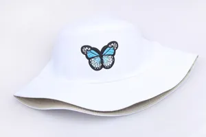 Ricamo dettagliato di farfalla blu su cappello pescatore bianco con cuciture rifinite