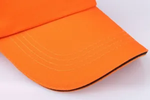 Detailed close-up of orange cotton baseball cap brim with precise stitching lines