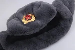 Detail of gray faux fur ushanka hat with Soviet metal badge showing hammer and sickle