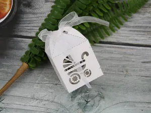 Close-up of white laser-cut baby stroller candy box with organza ribbon on wood table