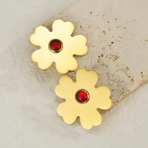 Gold stainless steel flower earrings with red gemstone inlay shown on a stone texture