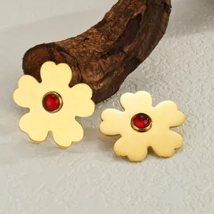 Golden flower earrings with red gemstone on natural wood background for women