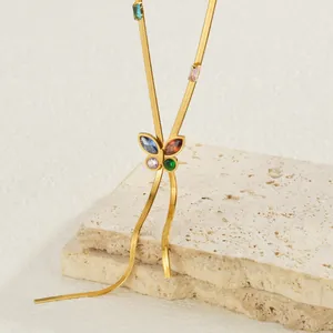 Gold butterfly necklace with colorful crystals and flat snake chain on stone surface